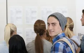 Male student smiling at camera while others read notice board